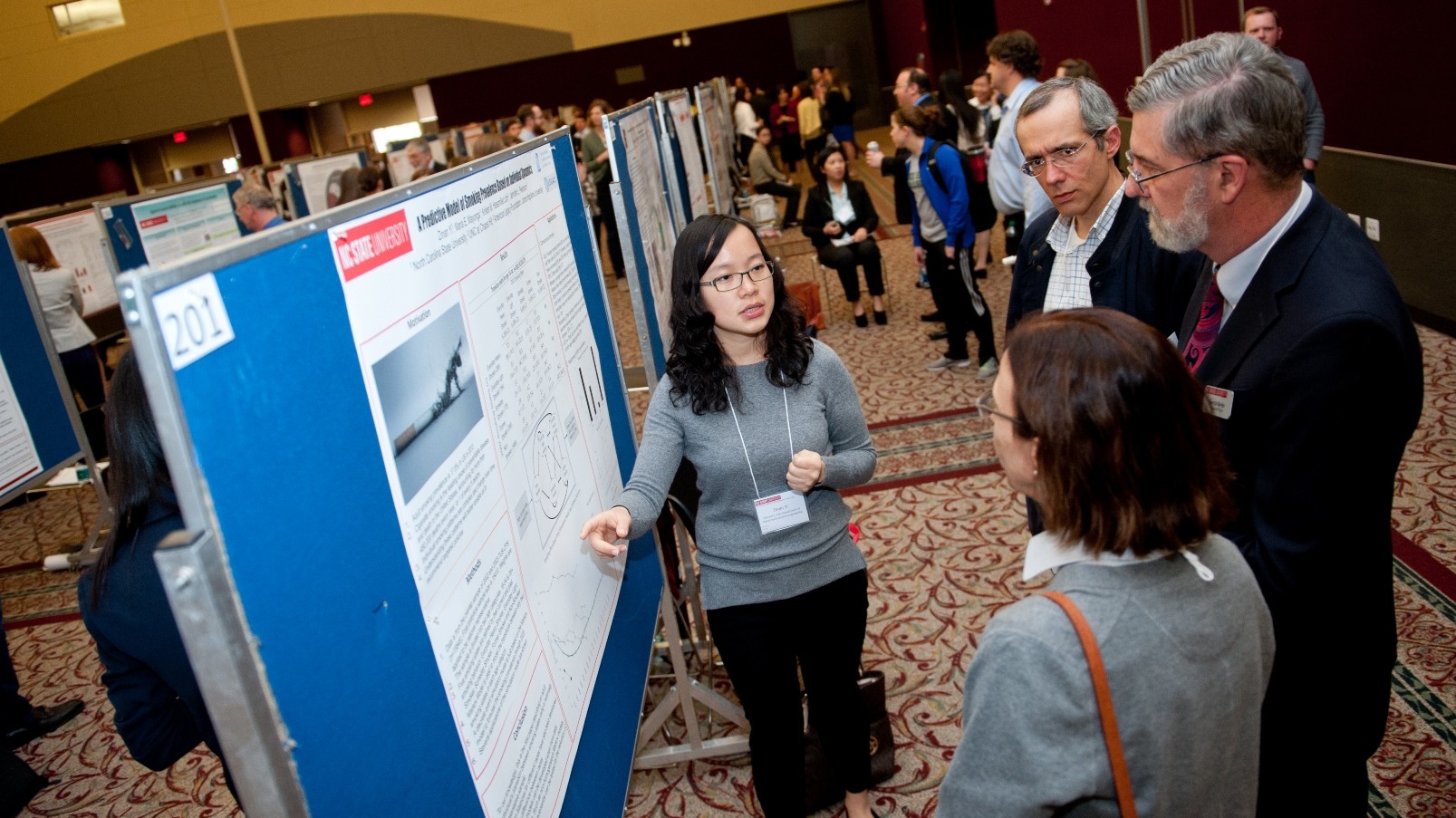 student explains poster to three people