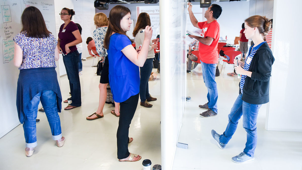 Image of writers participating in Camp Completion by standing up and writing on whiteboards in the Hunt Library Creativity Studio. They are "concept mapping" their dissertations.