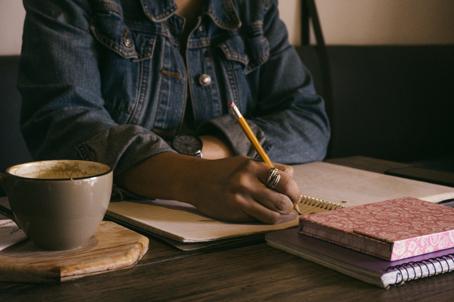 Person writing in a journal at a desk with coffee and other books