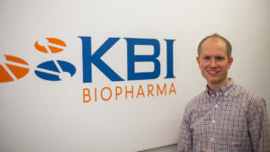 Dane Grismer with the KBI Biopharma logo on a wall