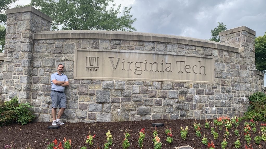 Tim Beck leaning against the Virginia Tech University stone welcome sign