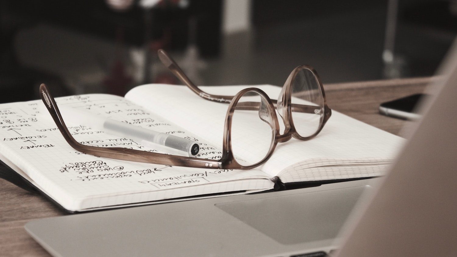 a pair of glasses resting on a journal with writing in it which is obscured