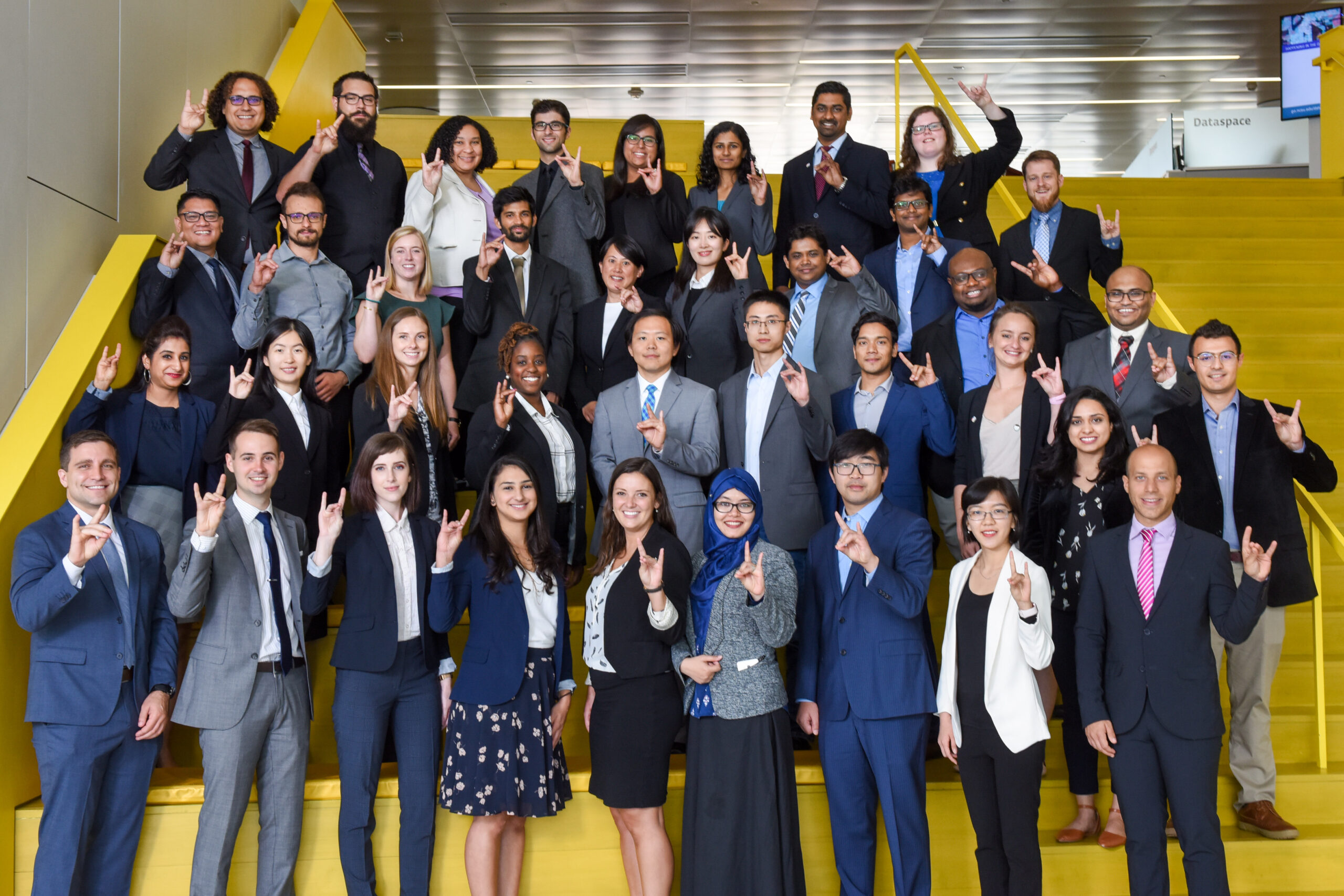 Group photo of Accelerate to Industry's Immersion Week participants holding up the pack sign.