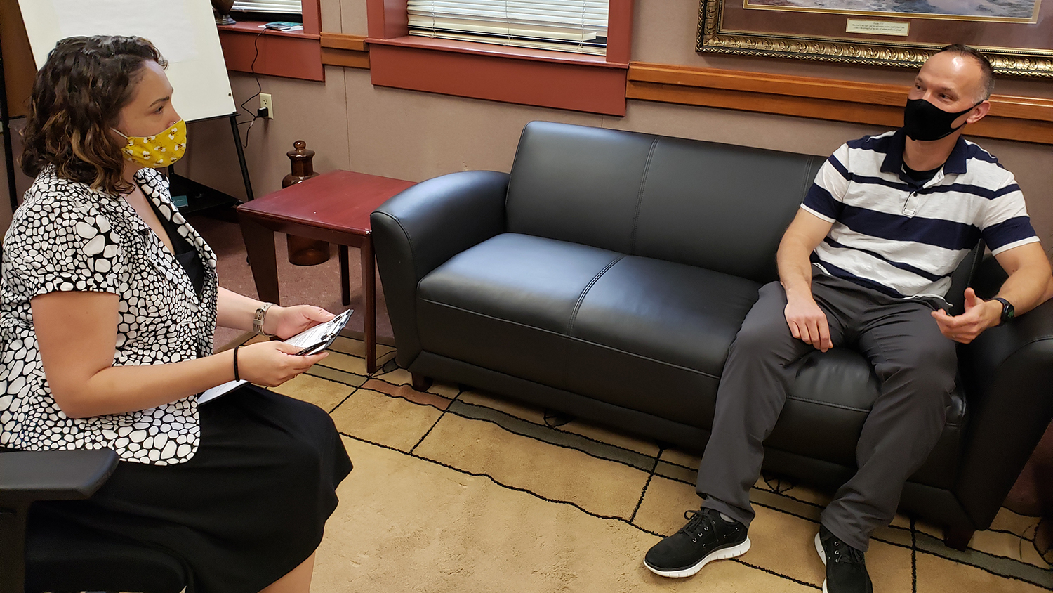 Sybil McCarrol sits with notepad and a client sits across the room on a couch.