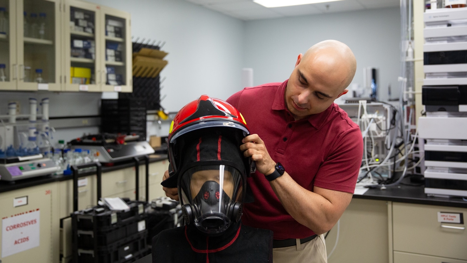 Arash Kasebi adjusts a firefighter helmet and hood on a mannequin head in a lab at the Wilson College of Textiles.
