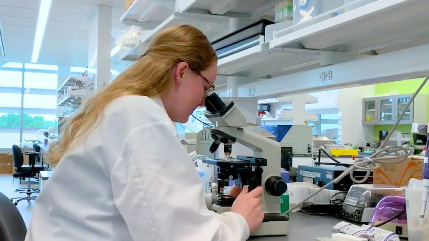 Micaela Robson wearing a white lab coat looking into a microscope