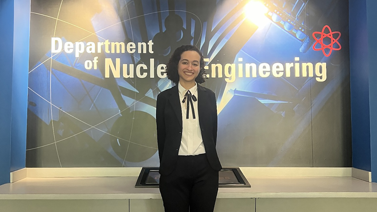 Dina Osama Elsayed Elgewaily in front of a large nuclear engineering display.