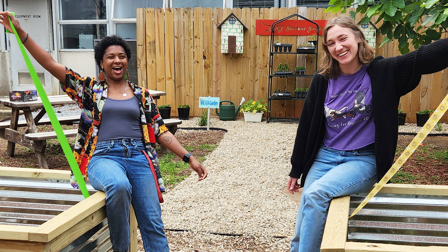Two young women sitting on garden planters laughing