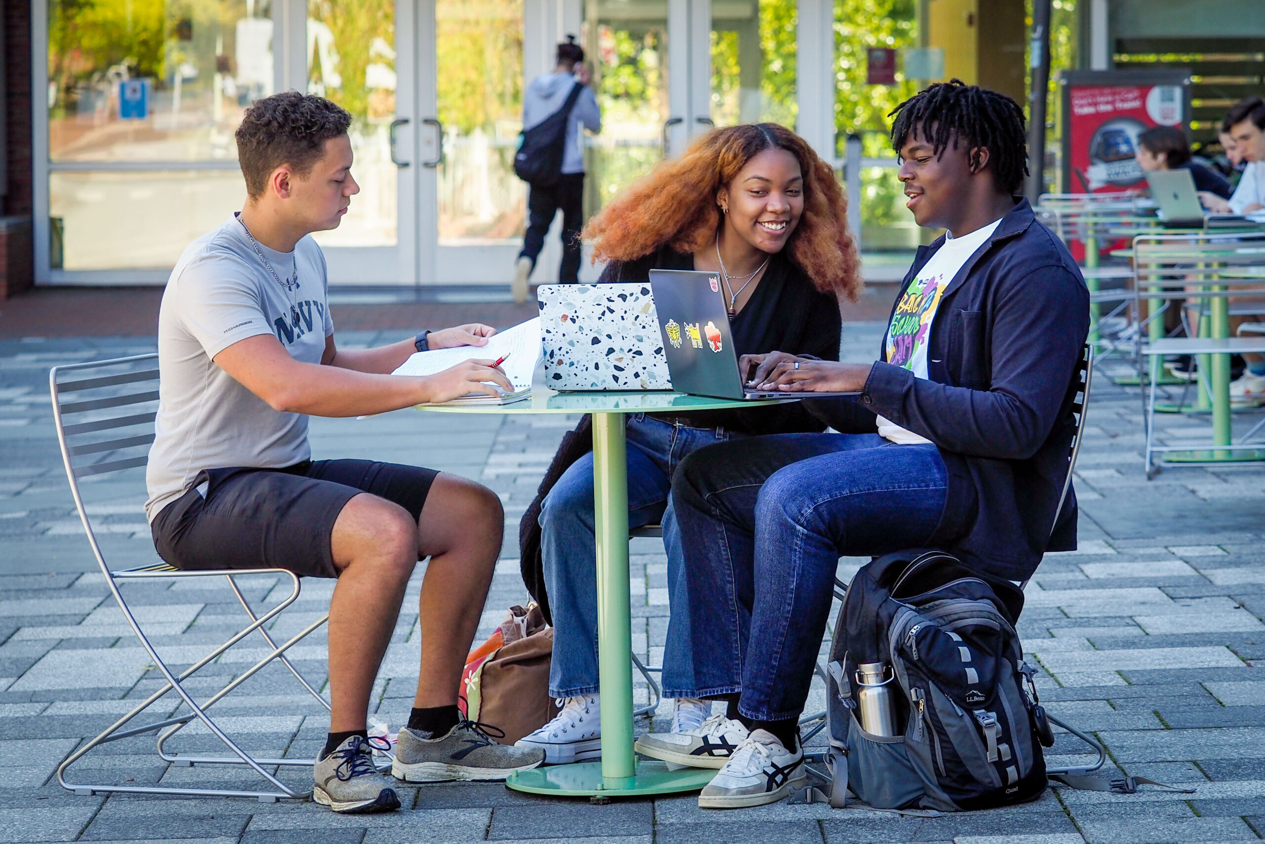 Three students sitting at a table outside working on laptops.