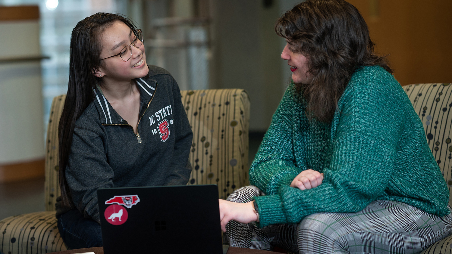 Two students chatting in front of a laptop